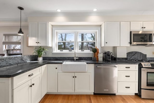 kitchen with light wood finished floors, a sink, ornamental molding, stainless steel appliances, and white cabinetry