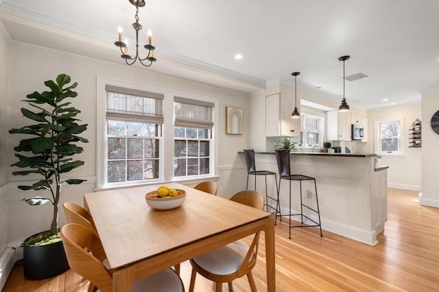 dining space with light wood-type flooring, baseboards, an inviting chandelier, and crown molding