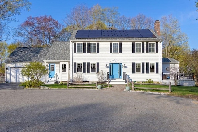 colonial inspired home featuring an attached garage, solar panels, a chimney, and entry steps
