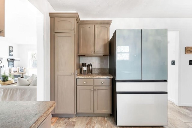 kitchen with freestanding refrigerator, light stone countertops, and tasteful backsplash