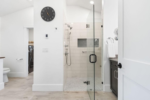 full bathroom featuring washer / dryer, wood finished floors, toilet, baseboards, and a shower stall