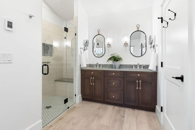 bathroom with double vanity, a sink, wood finished floors, and a stall shower