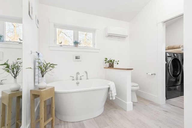 full bathroom featuring toilet, plenty of natural light, wood finished floors, a wall mounted AC, and a soaking tub