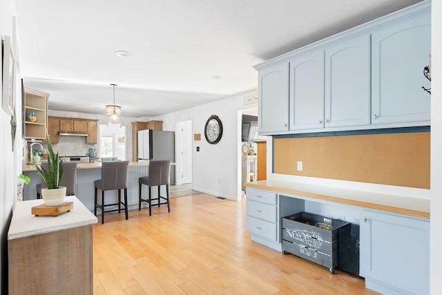 kitchen with light wood-style floors, light countertops, a kitchen breakfast bar, stainless steel appliances, and under cabinet range hood