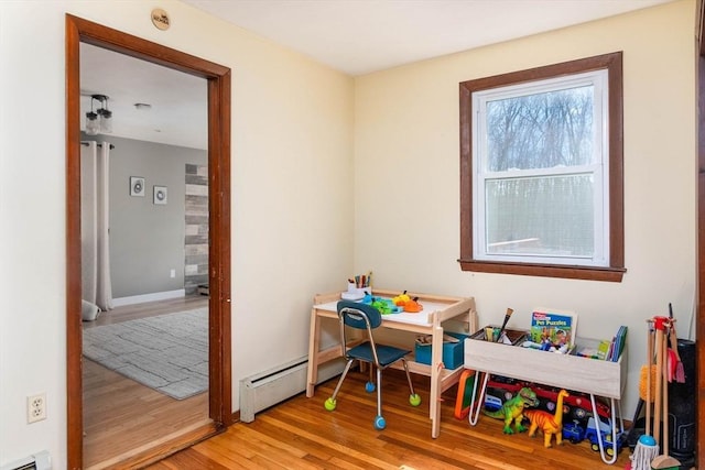 playroom with a baseboard heating unit, baseboards, and light wood-type flooring