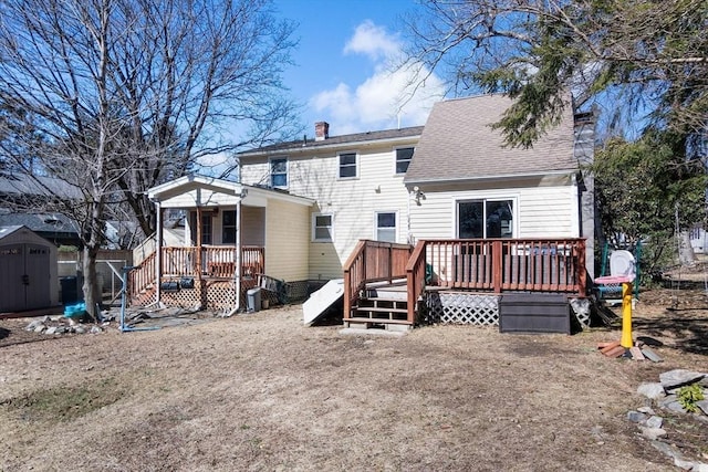 back of house featuring a shed, a wooden deck, roof with shingles, a chimney, and an outbuilding