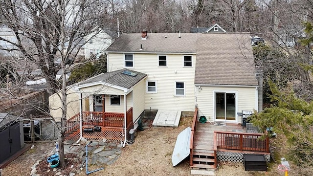 back of house with a chimney, a deck, and roof with shingles