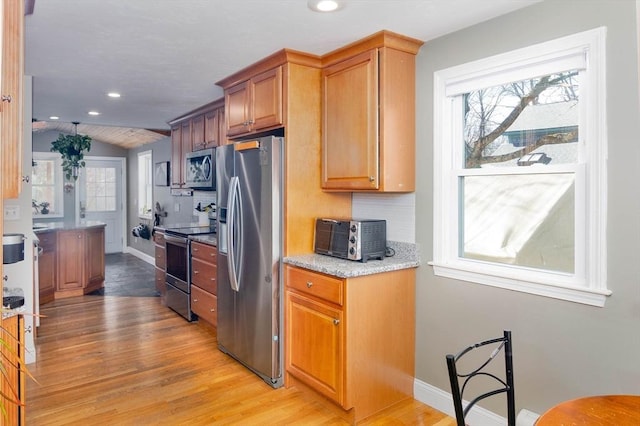 kitchen featuring a wealth of natural light, appliances with stainless steel finishes, light wood-type flooring, and vaulted ceiling