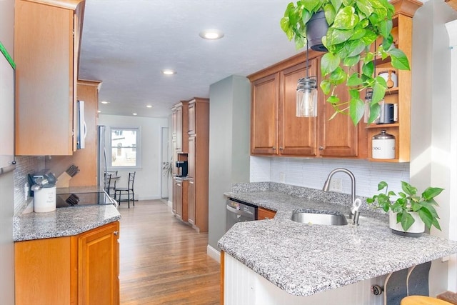 kitchen featuring light stone counters, brown cabinetry, a peninsula, light wood-style flooring, and a sink