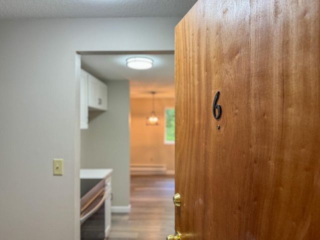 hallway featuring baseboards, a textured ceiling, wood finished floors, and a baseboard heating unit