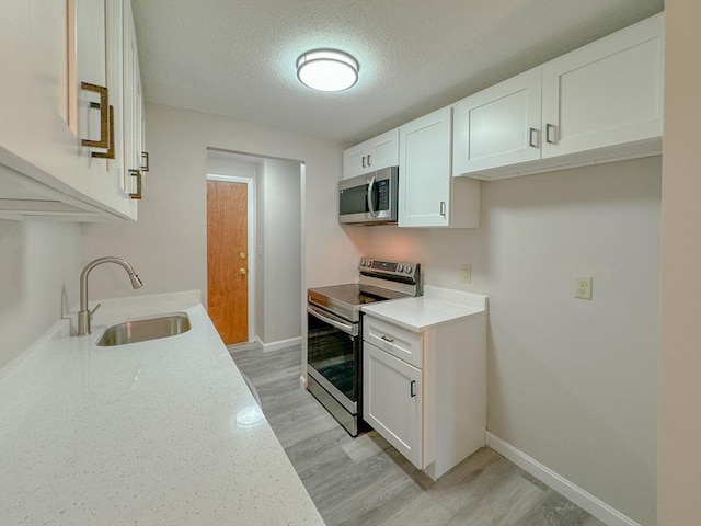 kitchen featuring white cabinetry, a textured ceiling, a sink, light wood-style flooring, and appliances with stainless steel finishes