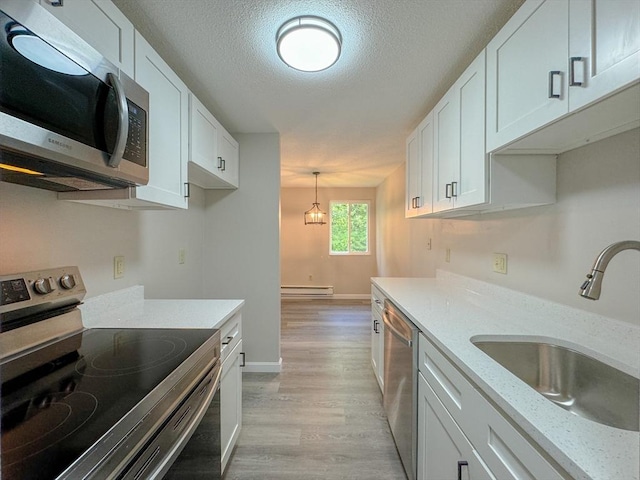 kitchen with a textured ceiling, white cabinets, appliances with stainless steel finishes, a sink, and light wood-style floors