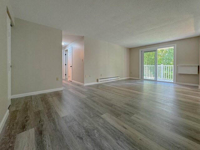 spare room with a textured ceiling, baseboards, a baseboard heating unit, and wood finished floors
