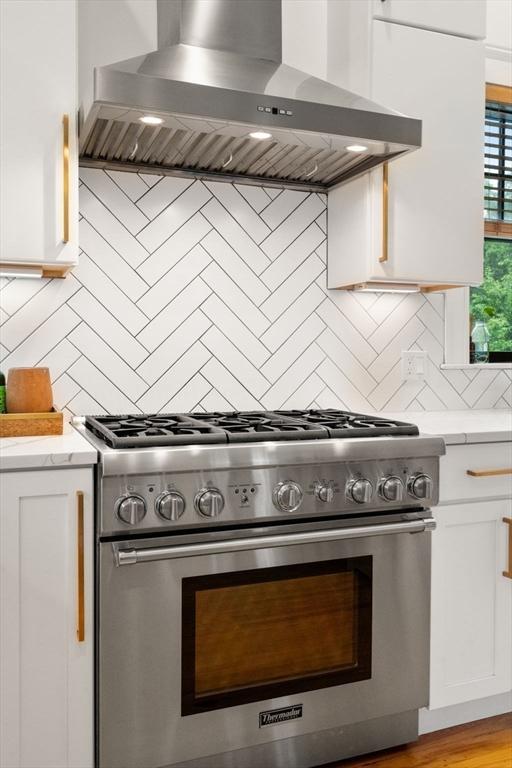 332 Eliot St, Milton, MA 02186 - kitchen with stainless steel stove, wall chimney exhaust hood, white cabinets, and tasteful backsplash