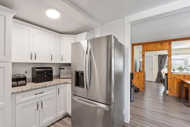 kitchen with stainless steel fridge, light stone counters, white cabinets, and light wood-type flooring
