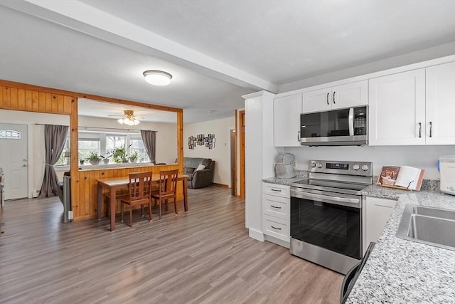 kitchen with appliances with stainless steel finishes, beam ceiling, a sink, white cabinets, and light wood-style flooring
