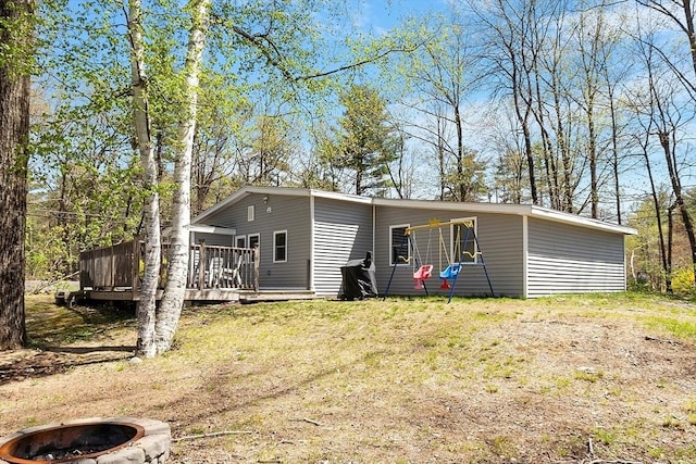 back of property with an outdoor fire pit, a wooden deck, and a yard