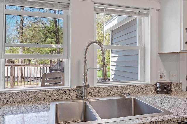 interior details featuring light stone counters, a sink, and white cabinets