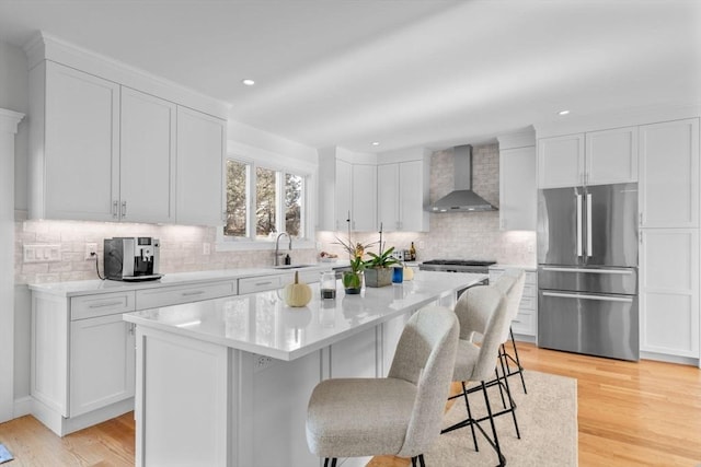 kitchen with a kitchen island, sink, wall chimney range hood, white cabinetry, and stainless steel refrigerator