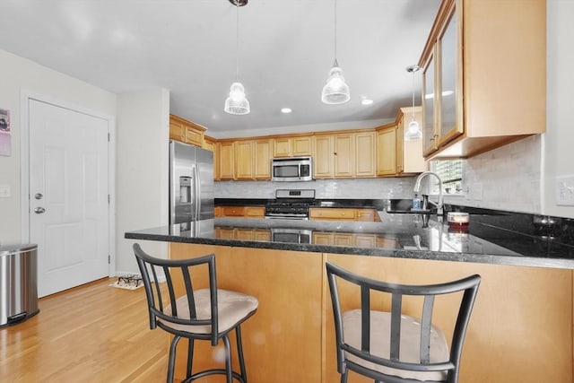 kitchen with stainless steel appliances, tasteful backsplash, light wood-style floors, a sink, and a peninsula