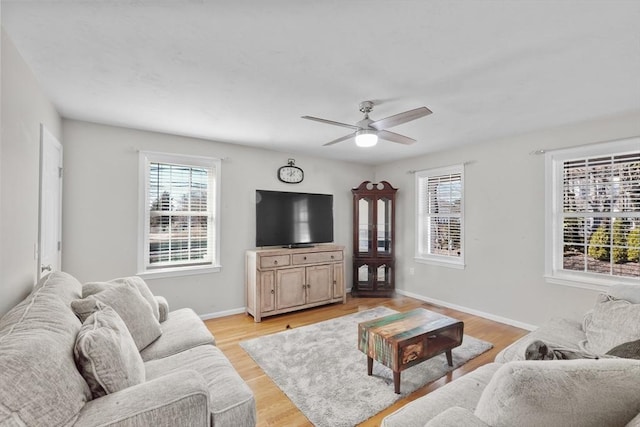 living area featuring a wealth of natural light, baseboards, ceiling fan, and light wood finished floors