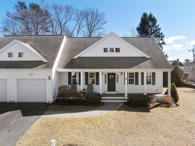 view of front of property featuring a shingled roof, aphalt driveway, an attached garage, covered porch, and a front yard