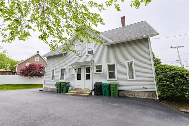 rear view of property featuring a chimney, roof with shingles, and fence