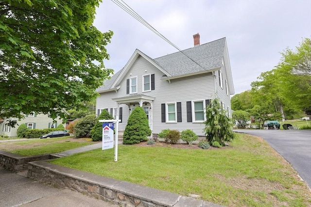 view of front of property with roof with shingles, a chimney, and a front yard