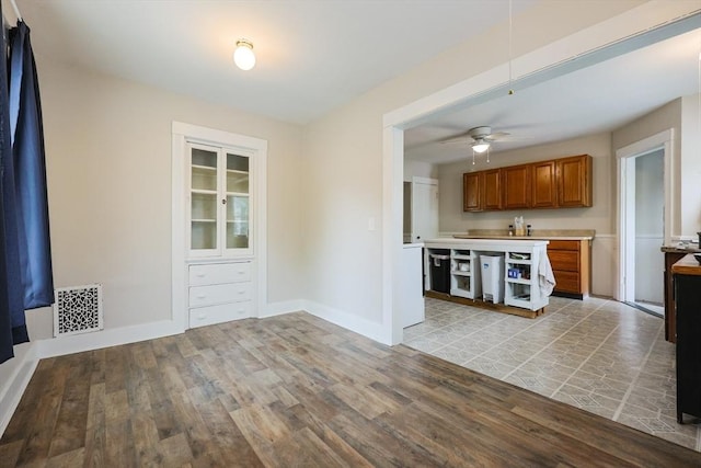 kitchen featuring brown cabinets, light wood-style floors, light countertops, a ceiling fan, and baseboards