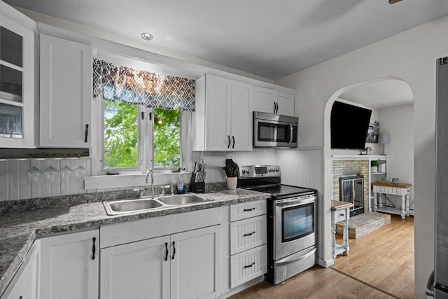 34 Coolidge St, Dartmouth, MA 02748 - kitchen with appliances with stainless steel finishes, a fireplace, white cabinetry, wood finished floors, and tasteful backsplash