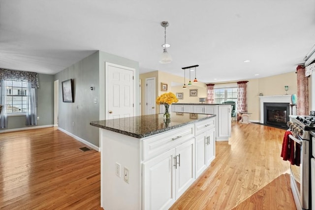 kitchen with dark stone countertops, stainless steel gas stove, a kitchen island, white cabinets, and decorative light fixtures