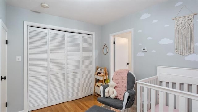 bedroom featuring a nursery area, a closet, and light wood-style floors