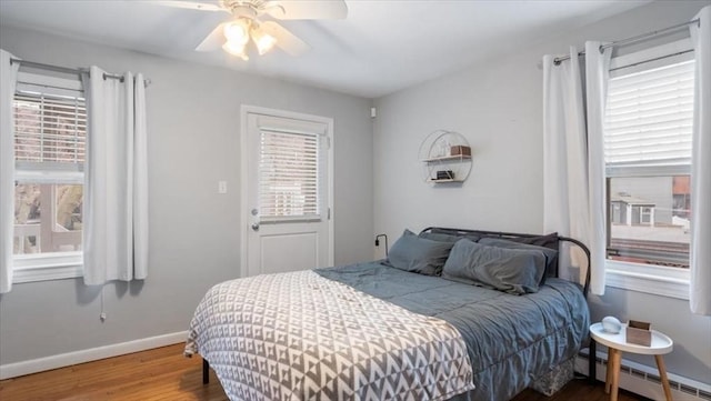 bedroom featuring a baseboard radiator, wood finished floors, a ceiling fan, and baseboards