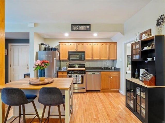 kitchen with stainless steel appliances, dark countertops, decorative backsplash, light wood-style floors, and a sink