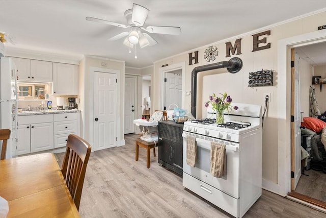 kitchen featuring light wood finished floors, white range with gas cooktop, crown molding, white cabinetry, and ceiling fan