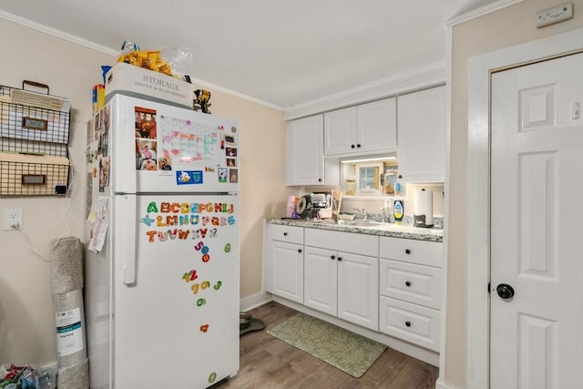 kitchen featuring freestanding refrigerator, ornamental molding, white cabinetry, and a sink