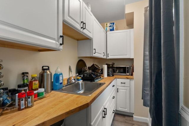 kitchen featuring wood counters, stainless steel microwave, a sink, and white cabinets