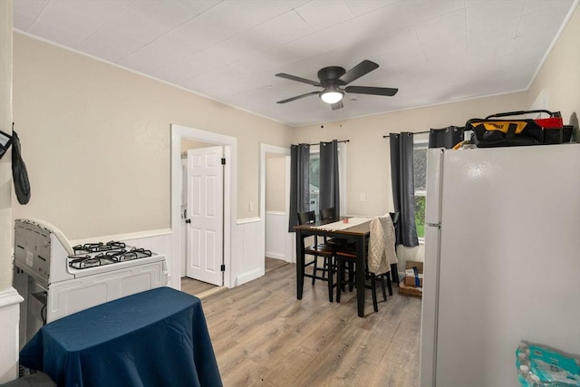 kitchen featuring freestanding refrigerator, ornamental molding, light wood-type flooring, ceiling fan, and wainscoting