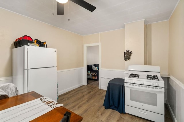 kitchen featuring light wood finished floors, a wainscoted wall, a ceiling fan, and white appliances