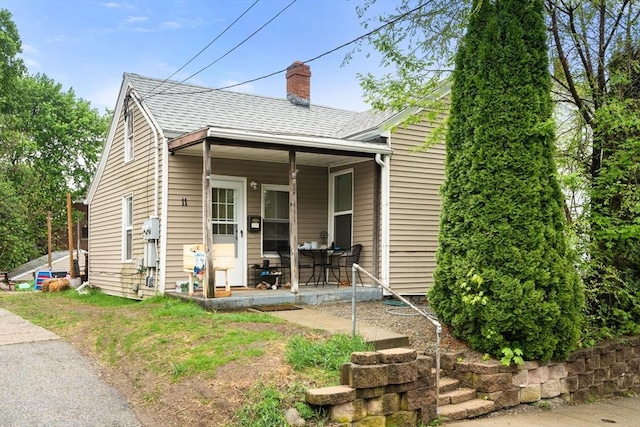 view of front of home with a chimney, roof with shingles, and covered porch