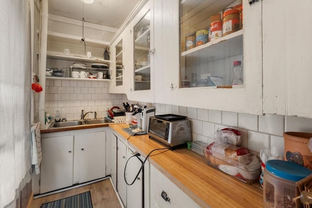 kitchen with a sink, butcher block countertops, light wood-style flooring, decorative backsplash, and white cabinets