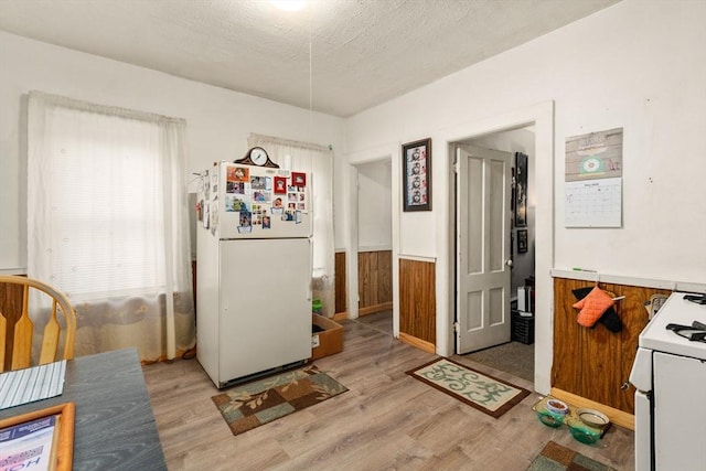 kitchen with white appliances, a wainscoted wall, a textured ceiling, light wood-type flooring, and light countertops