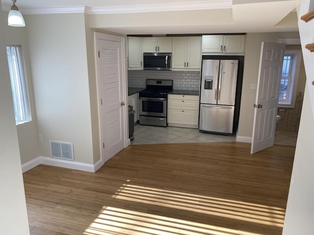 kitchen featuring appliances with stainless steel finishes, backsplash, hanging light fixtures, ornamental molding, and light hardwood / wood-style floors