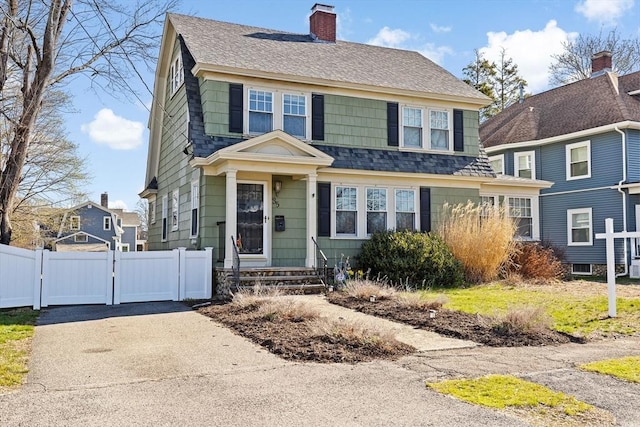 colonial inspired home featuring a chimney, a gate, fence, a shingled roof, and driveway