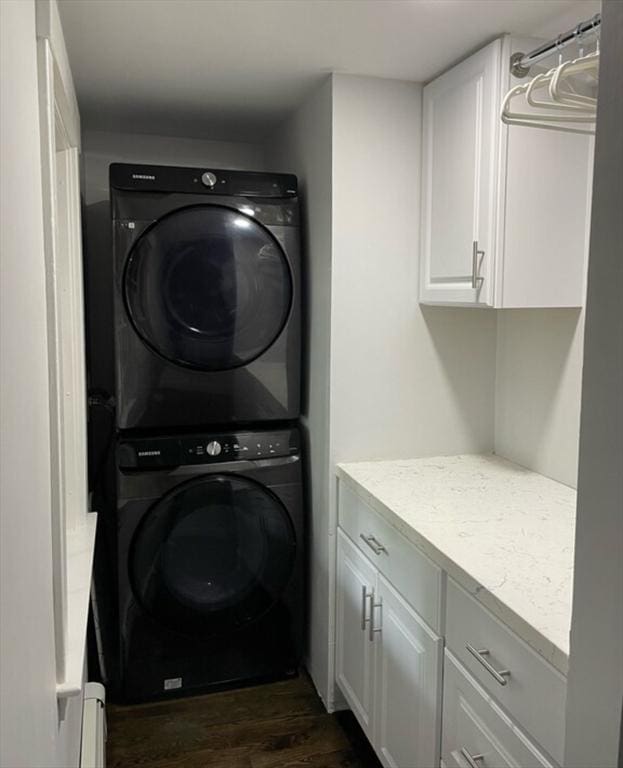 washroom featuring dark wood-type flooring, a baseboard radiator, stacked washing maching and dryer, and cabinets