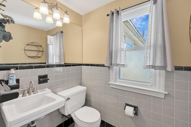 half bathroom featuring a sink, toilet, tile walls, and wainscoting