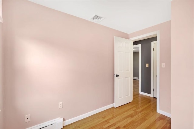 empty room featuring visible vents, baseboard heating, light wood-style floors, and baseboards