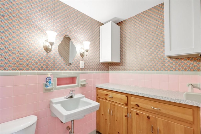 bathroom with wallpapered walls, toilet, a wainscoted wall, and a sink