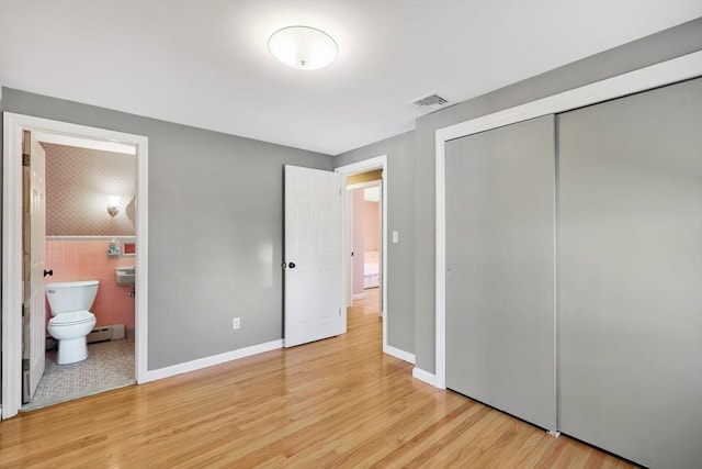 unfurnished bedroom featuring light wood-type flooring, visible vents, a closet, tile walls, and a baseboard radiator