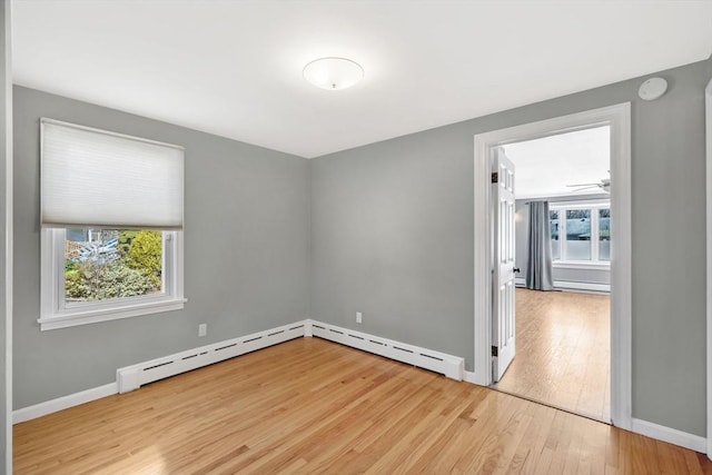 spare room with baseboard heating, a healthy amount of sunlight, baseboards, and hardwood / wood-style flooring